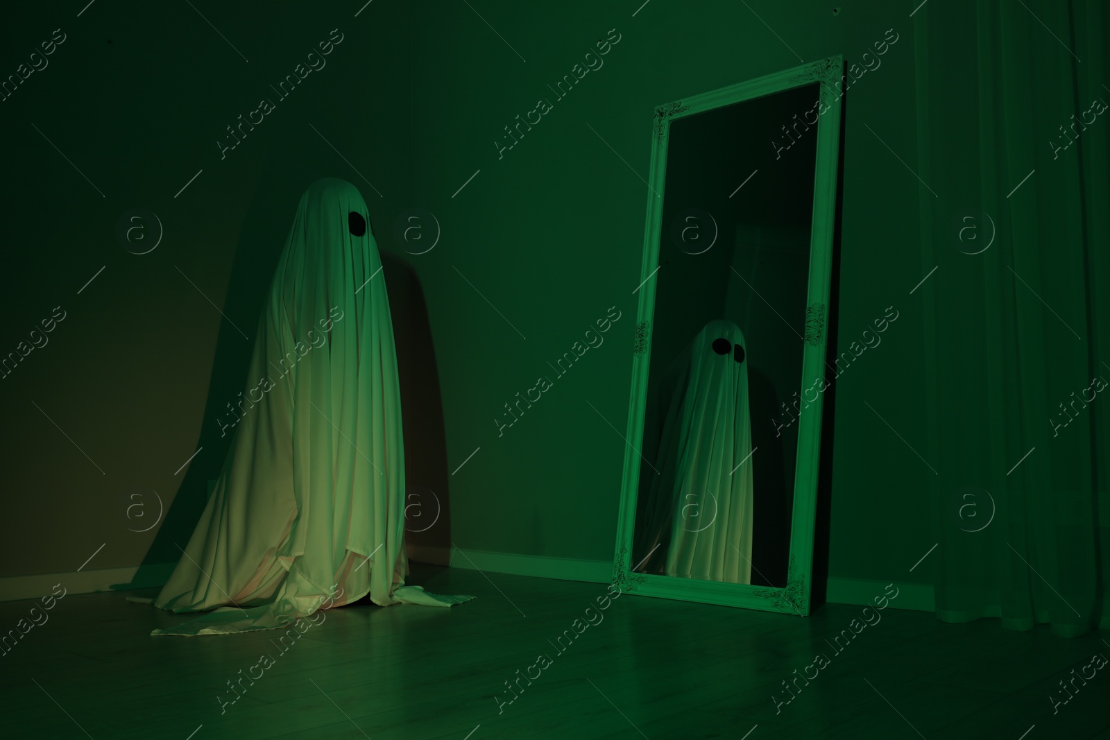 Photo of Creepy ghost. Woman covered with sheet looking at mirror in green light