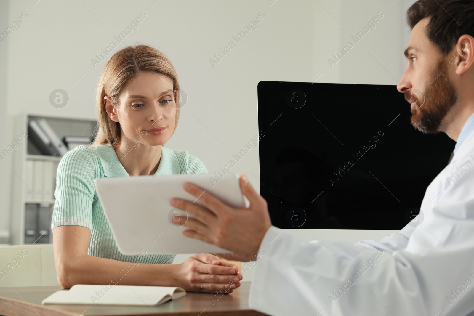 Photo of Doctor consulting patient at wooden table in clinic