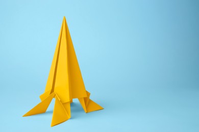 Photo of Origami art. Handmade yellow paper rocket on light blue background, space for text