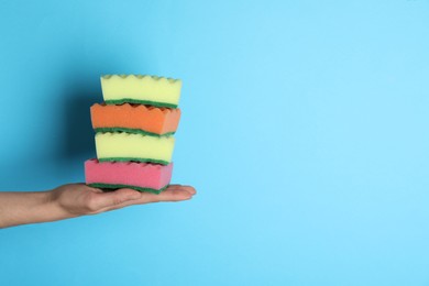 Woman holding sponges on light blue background, closeup. Space for text