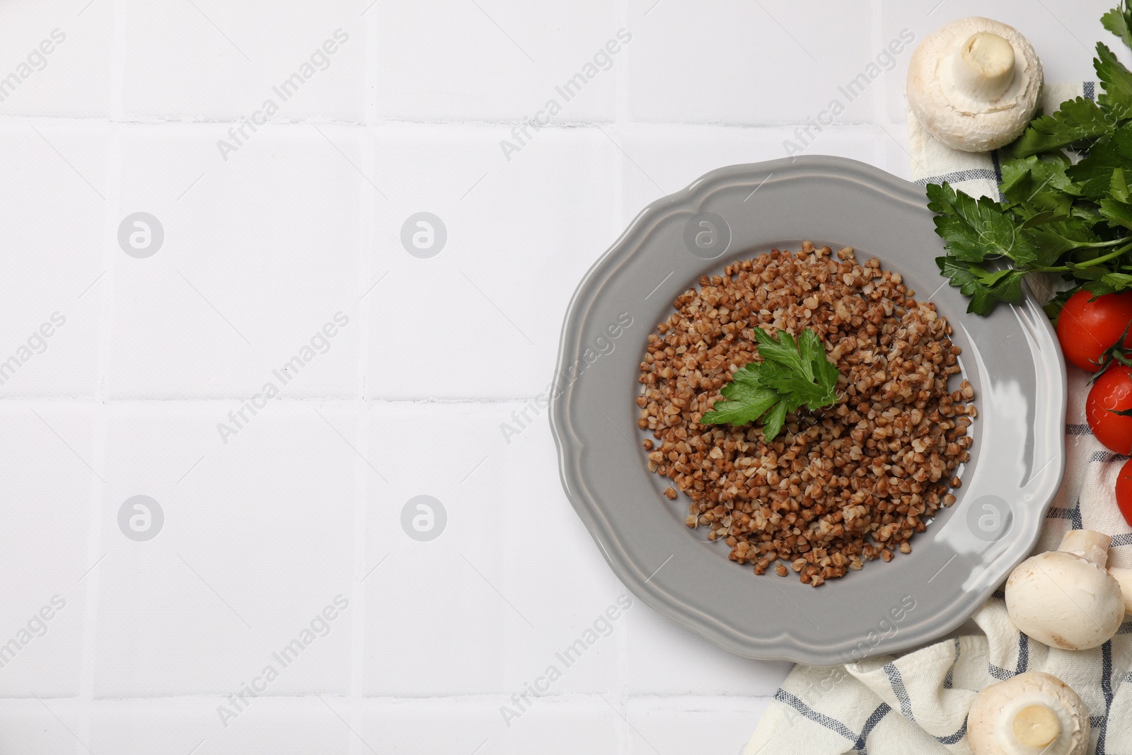 Photo of Tasty buckwheat with parsley on white tiled table, flat lay. Space for text