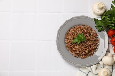 Photo of Tasty buckwheat with parsley on white tiled table, flat lay. Space for text