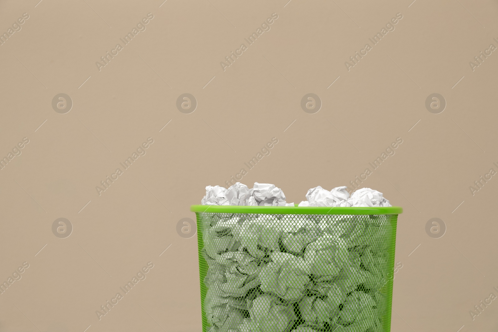 Photo of Metal bin with crumpled paper against color background, space for text