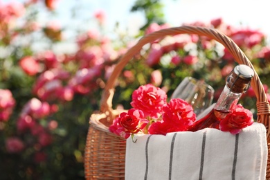 Wicker basket with bottle of wine and roses outdoors, space for text