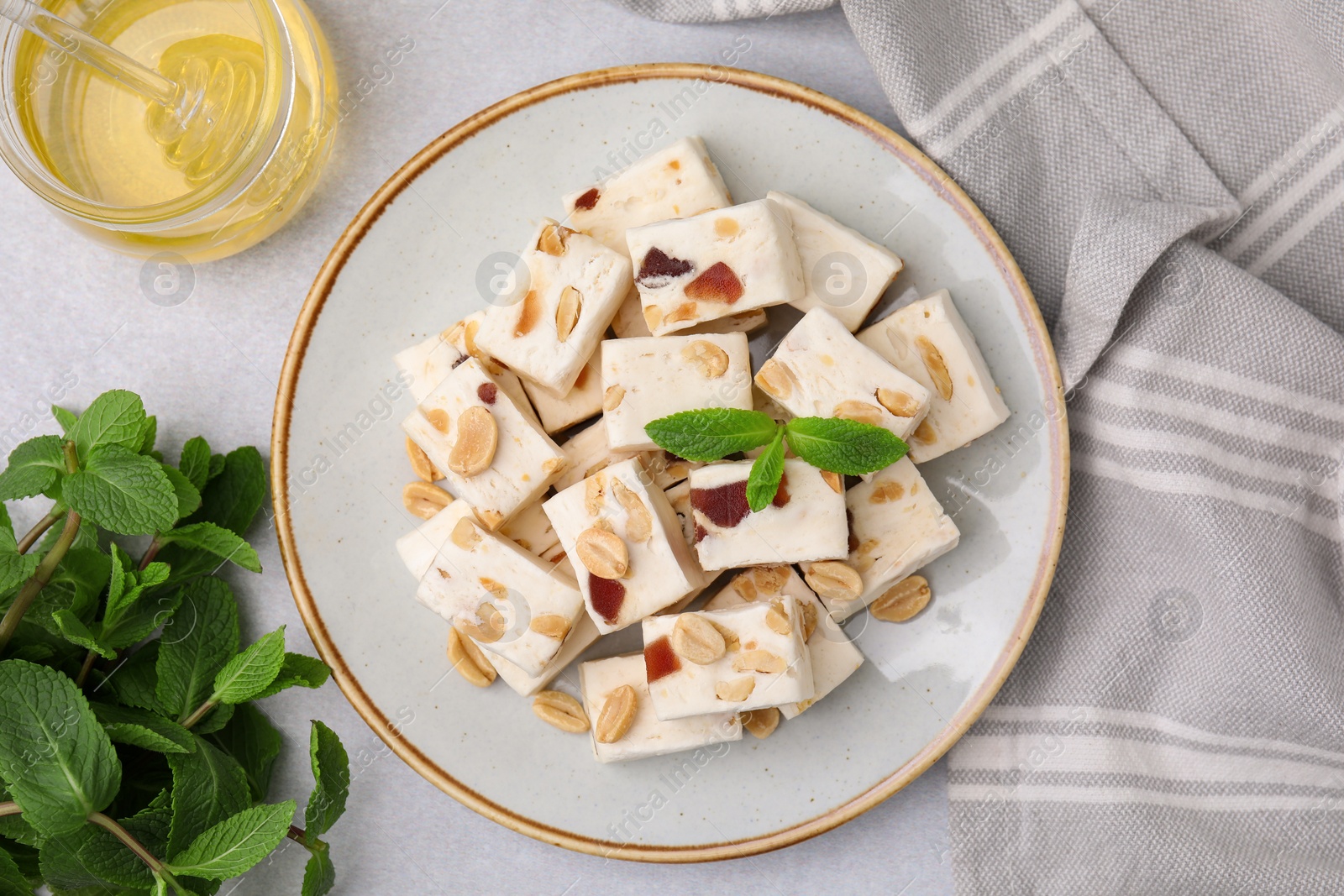 Photo of Pieces of delicious nutty nougat, mint and honey on light table, flat lay