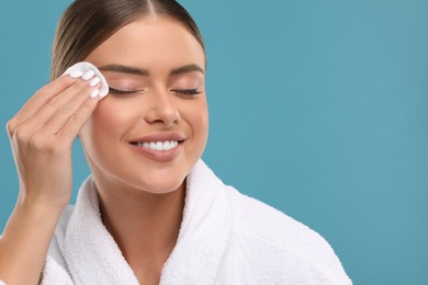 Beautiful woman removing makeup with cotton pad on light blue background, space for text