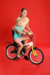 Photo of Young mother teaching daughter to ride bicycle on red background