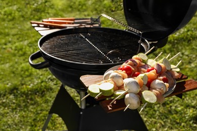 Photo of Skewers with meat and vegetables near barbecue grill outdoors