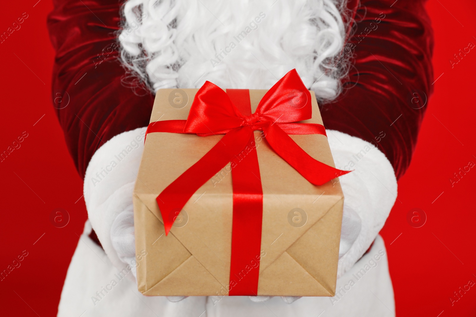 Photo of Santa Claus holding Christmas gift on red background, closeup