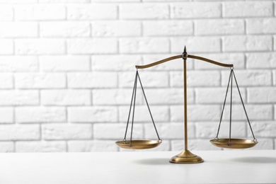 Photo of Scales of justice on table against brick wall. Law concept