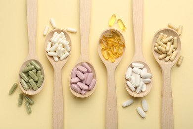 Photo of Different vitamin pills in spoons on pale yellow background, flat lay
