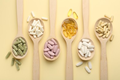 Different vitamin pills in spoons on pale yellow background, flat lay