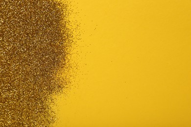 Photo of Shiny golden glitter on yellow background, top view. Space for text