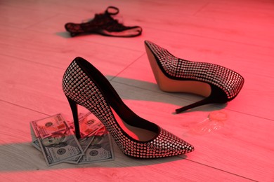 Prostitution concept. High heeled shoes and dollar banknotes on floor in neon light