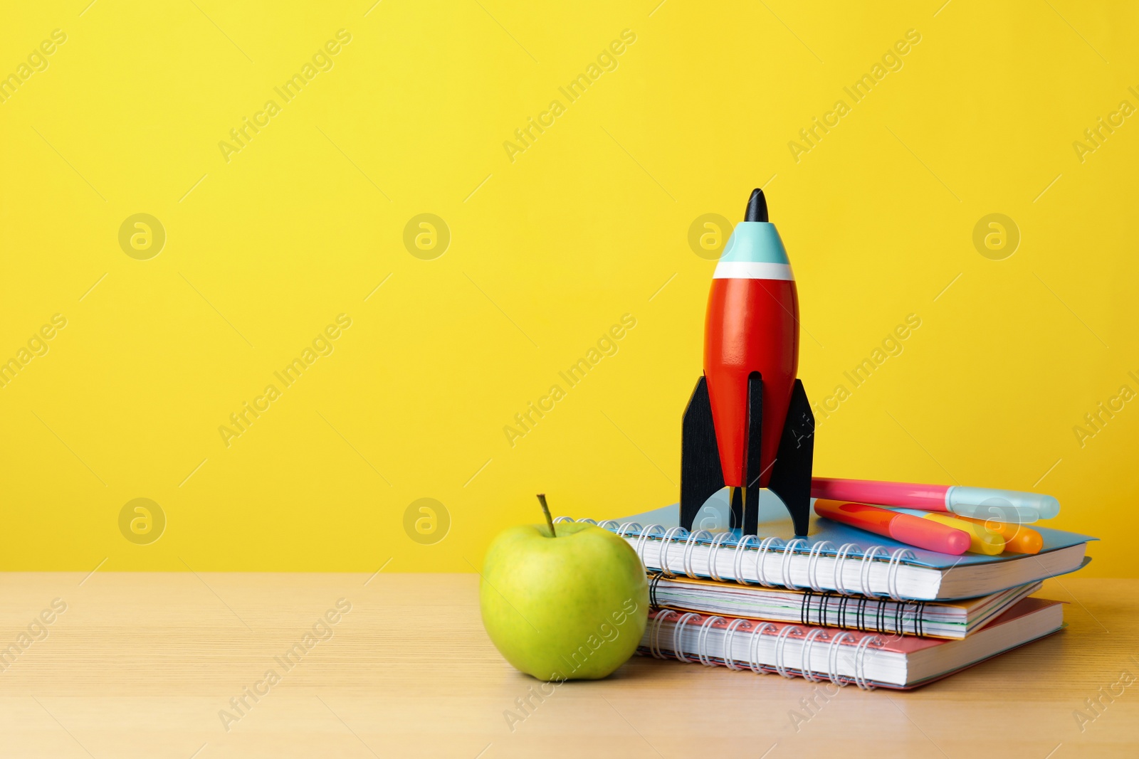 Photo of Bright toy rocket and school supplies on wooden table. Space for text