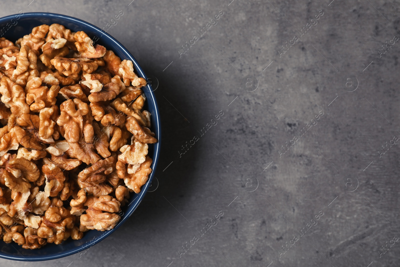 Photo of Dish with walnuts on grey background, top view. Space for text