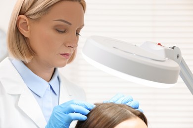 Trichologist examining patient`s hair under lamp in clinic