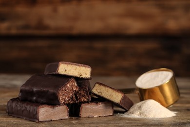 Photo of Pieces of tasty bars and scoop with protein powder on wooden table. Space for text