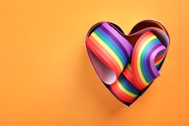 Heart shaped mold and bright rainbow ribbon on color background, top view with space for text. Symbol of gay community