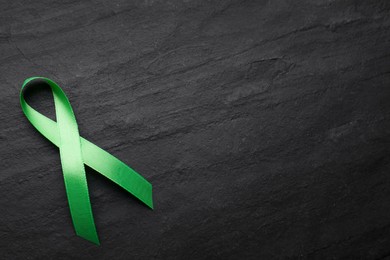 World Mental Health Day. Green ribbon on black background, top view with space for text