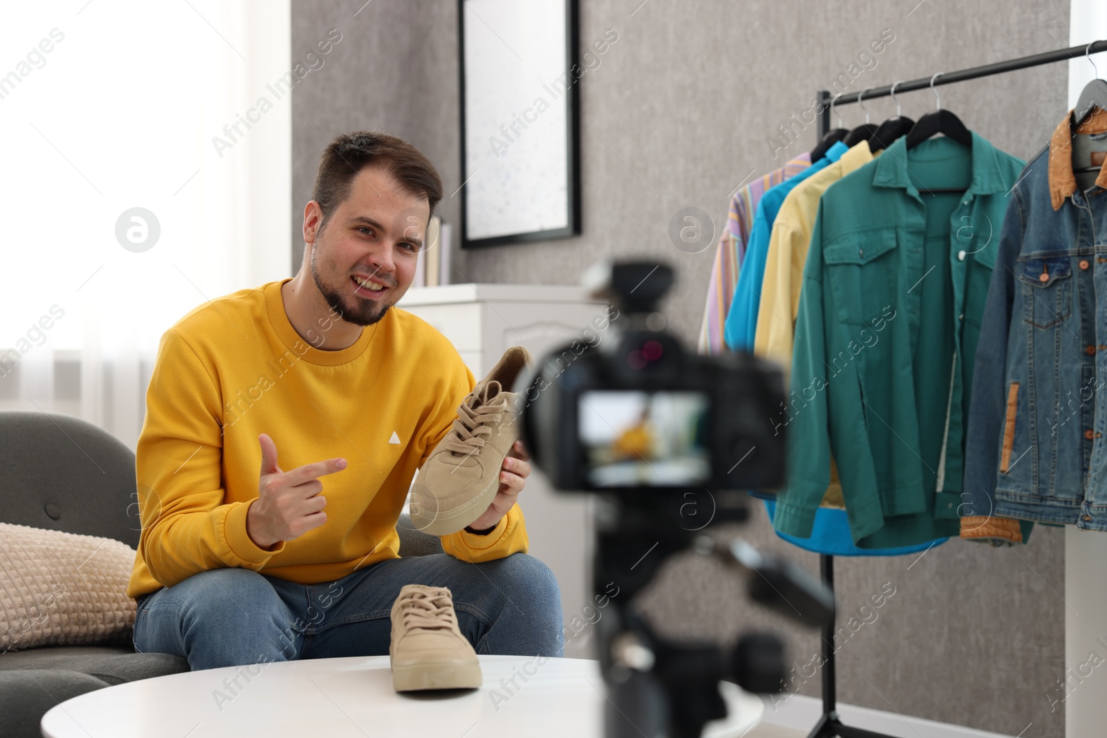 Photo of Smiling fashion blogger showing shoes while recording video at home