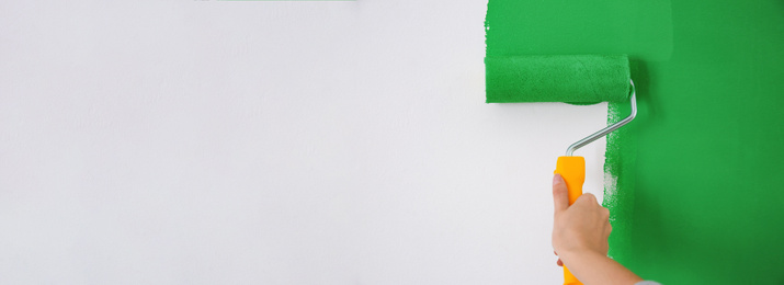 Professional decorator painting white wall with green dye, space for text. Banner design
