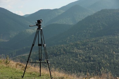 Photo of Tripod with modern camera in mountains on sunny day. Space for text