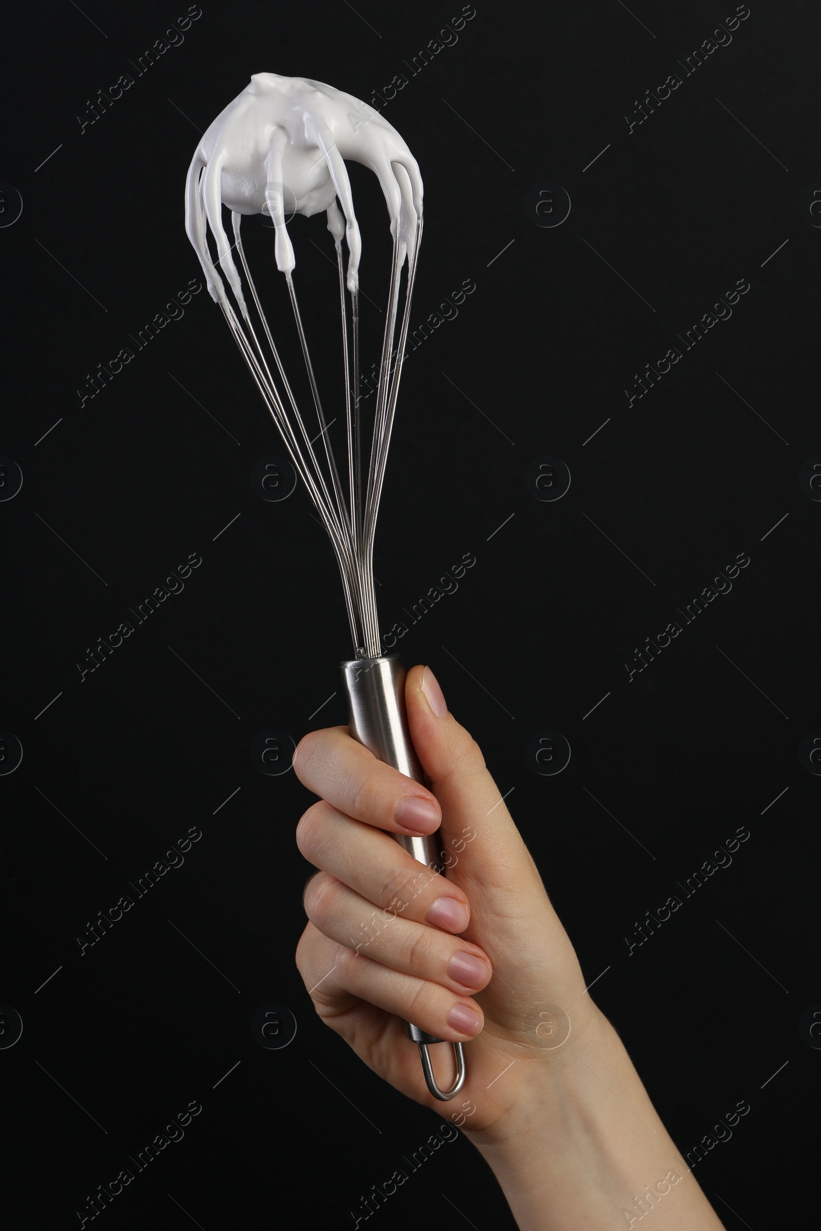 Photo of Woman holding whisk with whipped cream on black background, closeup