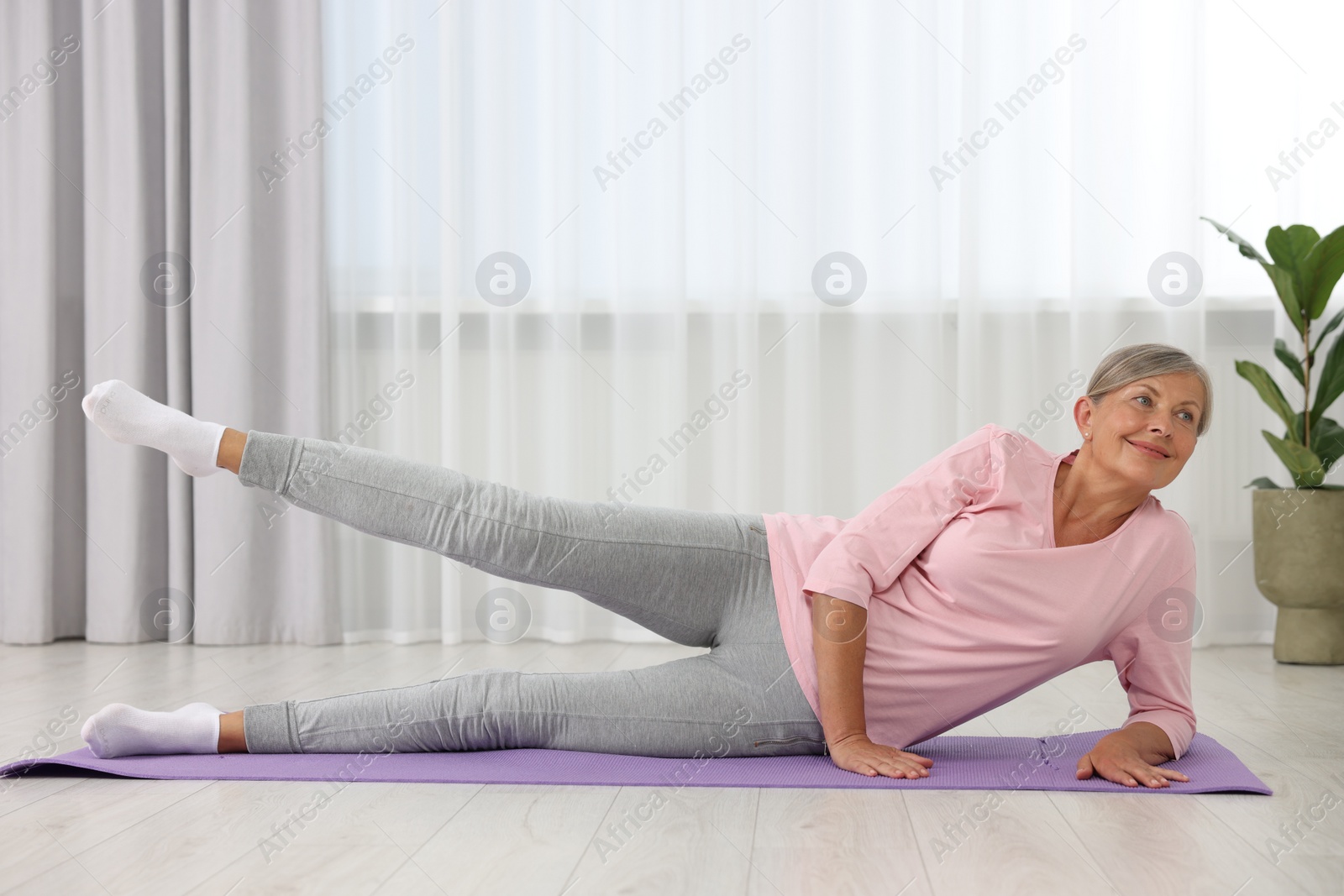 Photo of Happy senior woman practicing yoga on mat at home