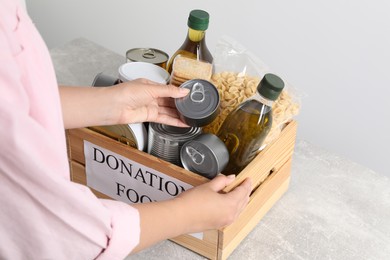 Photo of Woman taking tin can out from donation crate at grey table, closeup