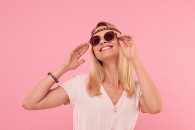 Portrait of smiling hippie woman in sunglasses on pink background