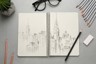 Image of Sketch of cityscape in notebook, pencils, eraser and glasses on grey table, flat lay