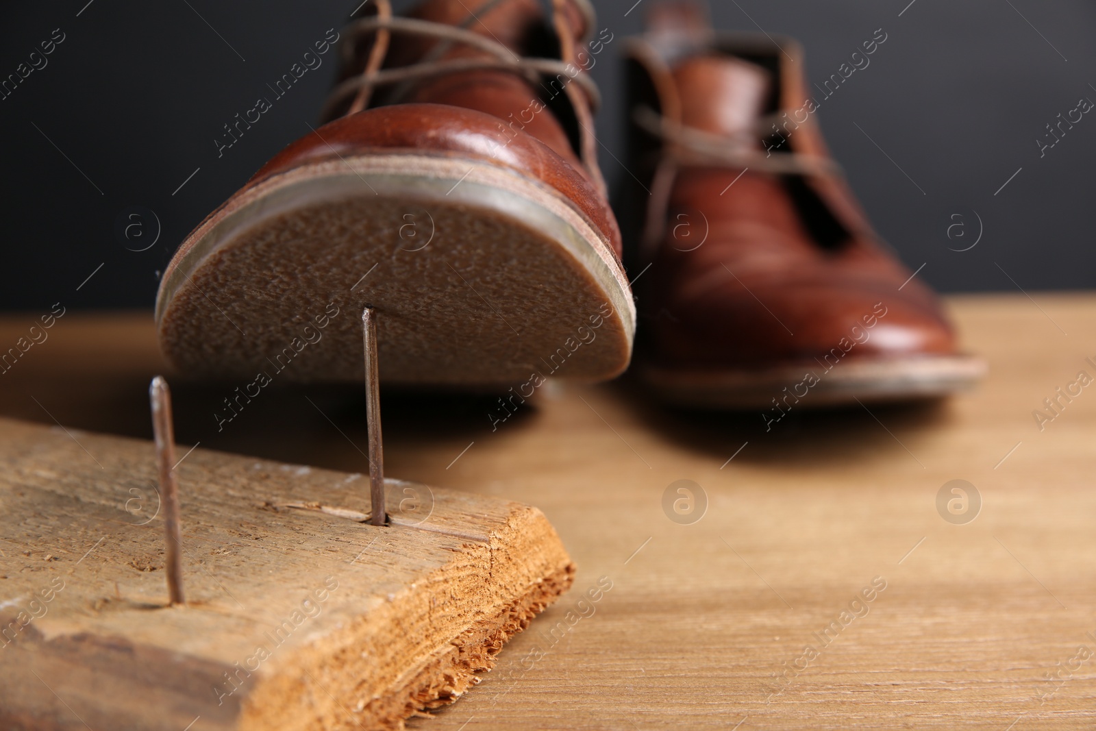 Photo of Metal nails in wooden plank and shoes on table, closeup