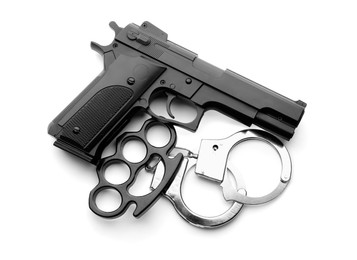 Photo of Black brass knuckles, gun and handcuffs on white background, top view
