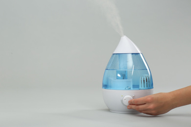 Woman using modern air humidifier on light grey background, closeup. Space for text