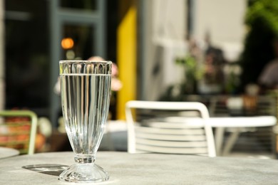 Glass of fresh water on light grey table outdoors. Space for text