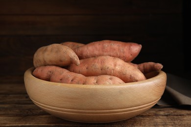 Photo of Fresh whole sweet potatoes in bowl on wooden table