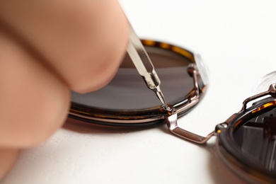 Photo of Handyman repairing sunglasses with screwdriver on white background, closeup