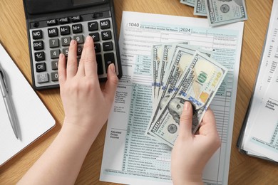 Payroll. Woman with dollar banknotes and calculator planning budget at wooden table, top view