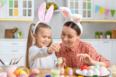 Photo of Mother and her cute daughter painting Easter eggs at table in kitchen