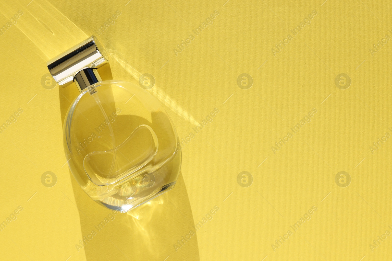 Photo of Luxury women's perfume. Sunlit glass bottle on yellow background, top view. Space for text