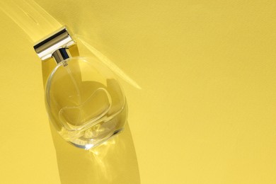 Photo of Luxury women's perfume. Sunlit glass bottle on yellow background, top view. Space for text