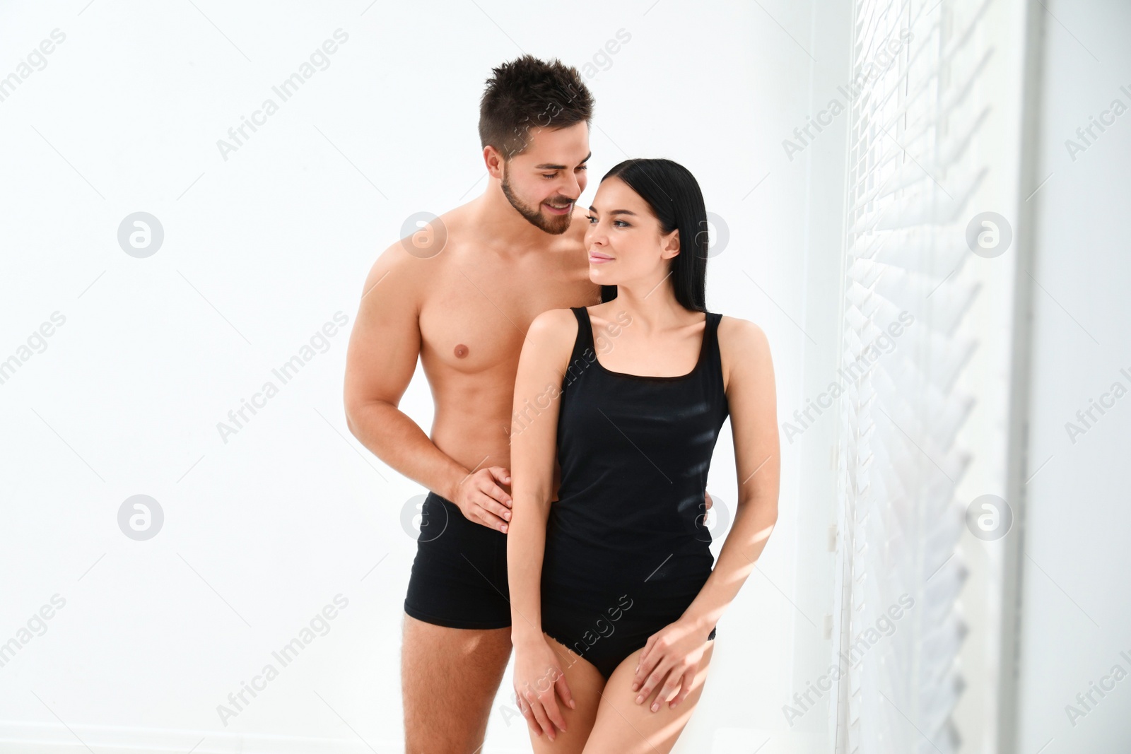 Photo of Young couple in black underwear near window indoors