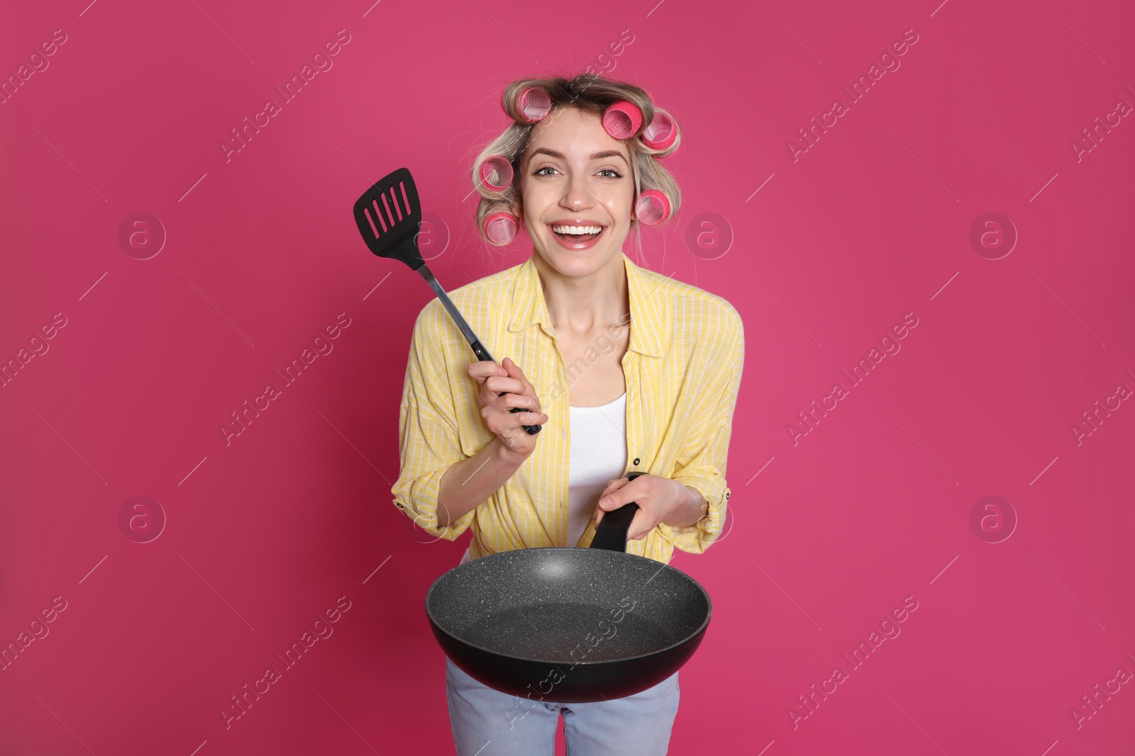 Photo of Young housewife with frying pan and spatula on pink background