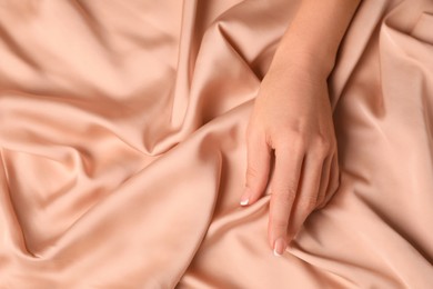 Photo of Woman touching smooth silky beige fabric, closeup