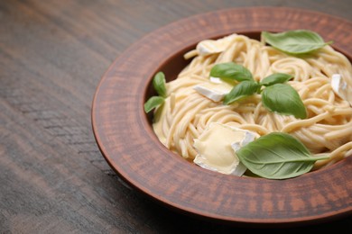 Delicious pasta with brie cheese and basil leaves on wooden table, closeup. Space for text