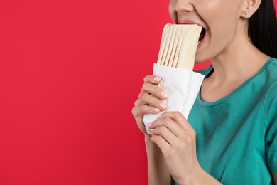 Photo of Young woman eating delicious shawarma on red background, closeup. Space for text