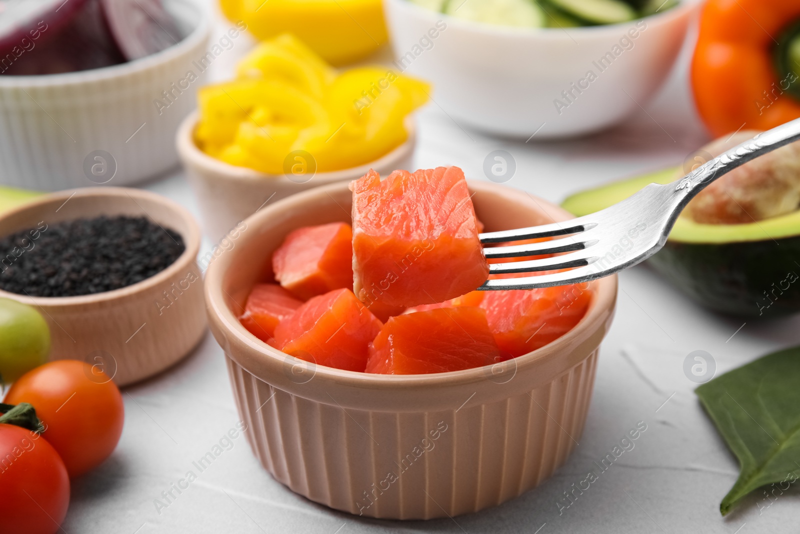 Photo of Holding salmon on fork at white table, closeup. Preparing poke bowl