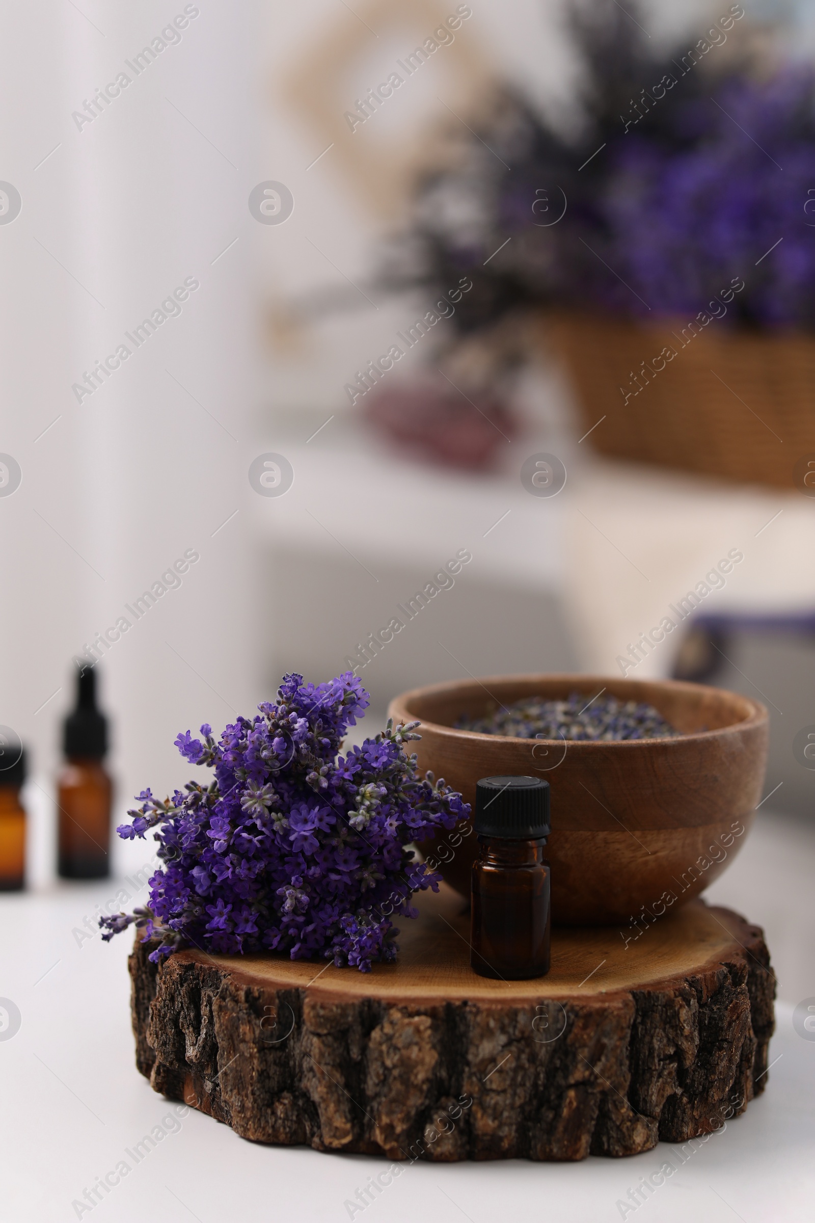 Photo of Bottle of aromatic essential oil and stump with beautiful flowers on white table indoors