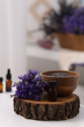 Bottle of aromatic essential oil and stump with beautiful flowers on white table indoors